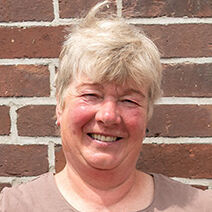 Die stolze Weiterbildungsteilnehmerin Astrid Estel steht, die Hände auf die Hüften gestützt, vor einer geziegelten Hauswand.