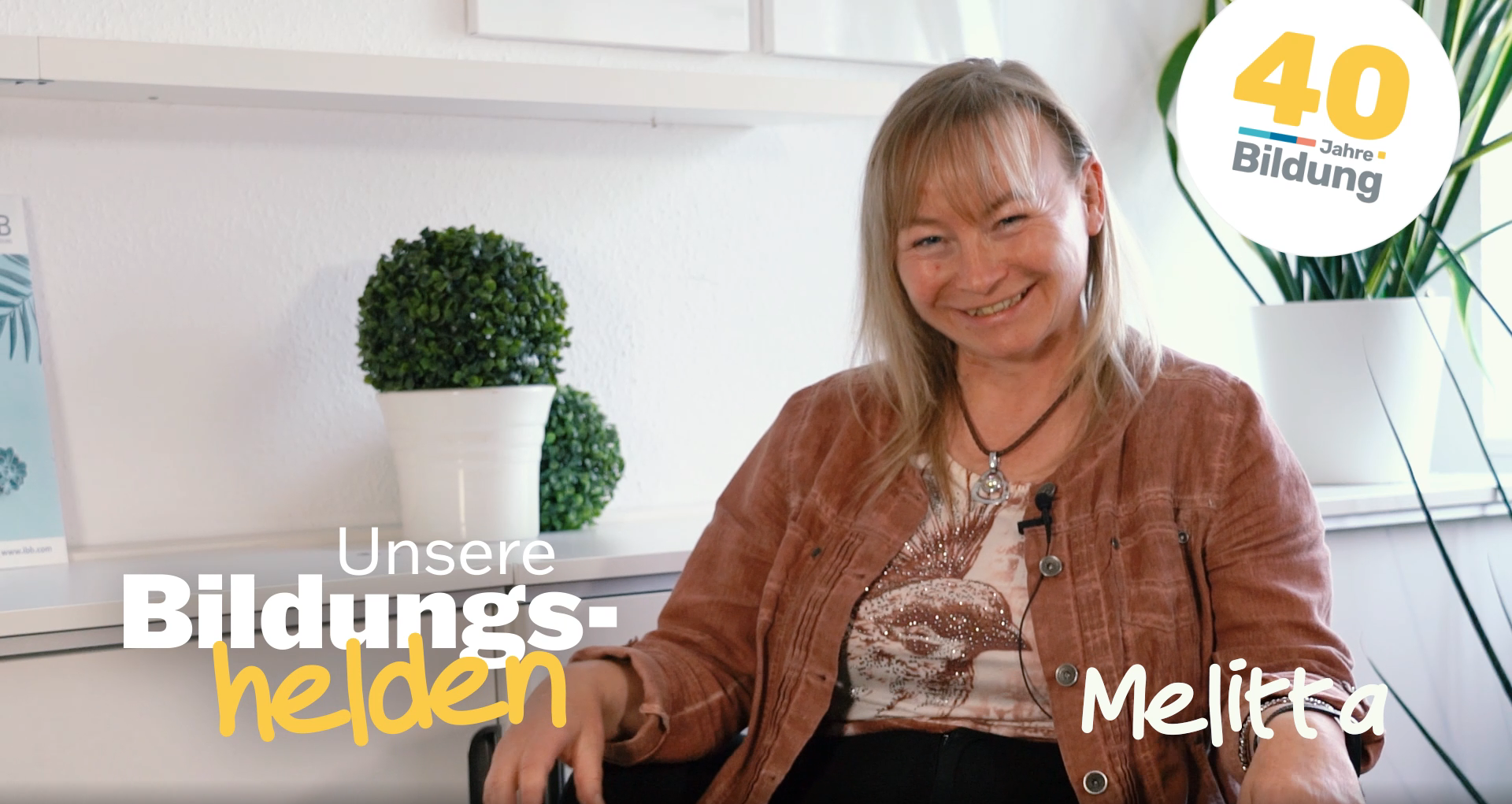 Video-Vorschaubild aus der Reihe "40 Jahre IBB - Bildungshelden": Melitta Vogenauer, IBB-Weiterbildungsteilnehmerin, sitzt glücklich lächelnd in einer bequemen Sitzecke am IBB-Standort in Stendal.